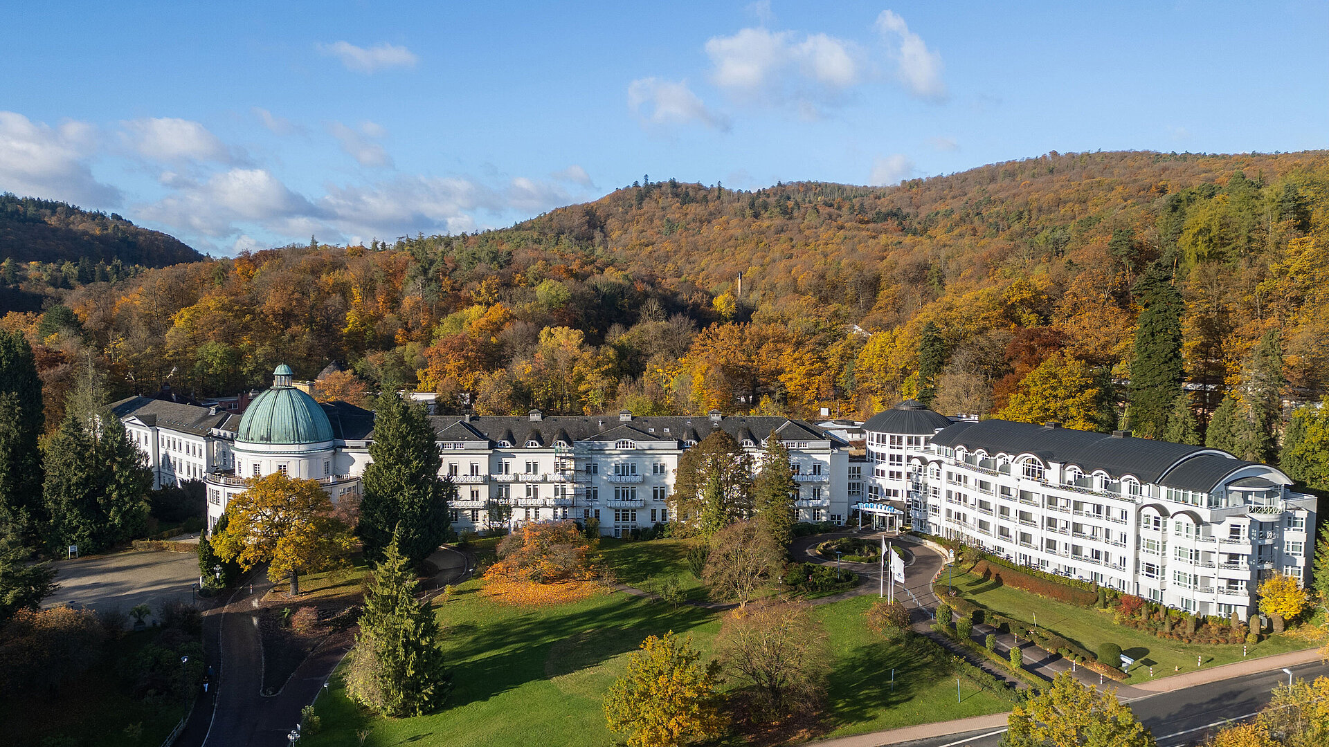 Exterior view of the Maritim Hotel Bad Wildungen surrounded by park, trees and an autumn forest panorama.