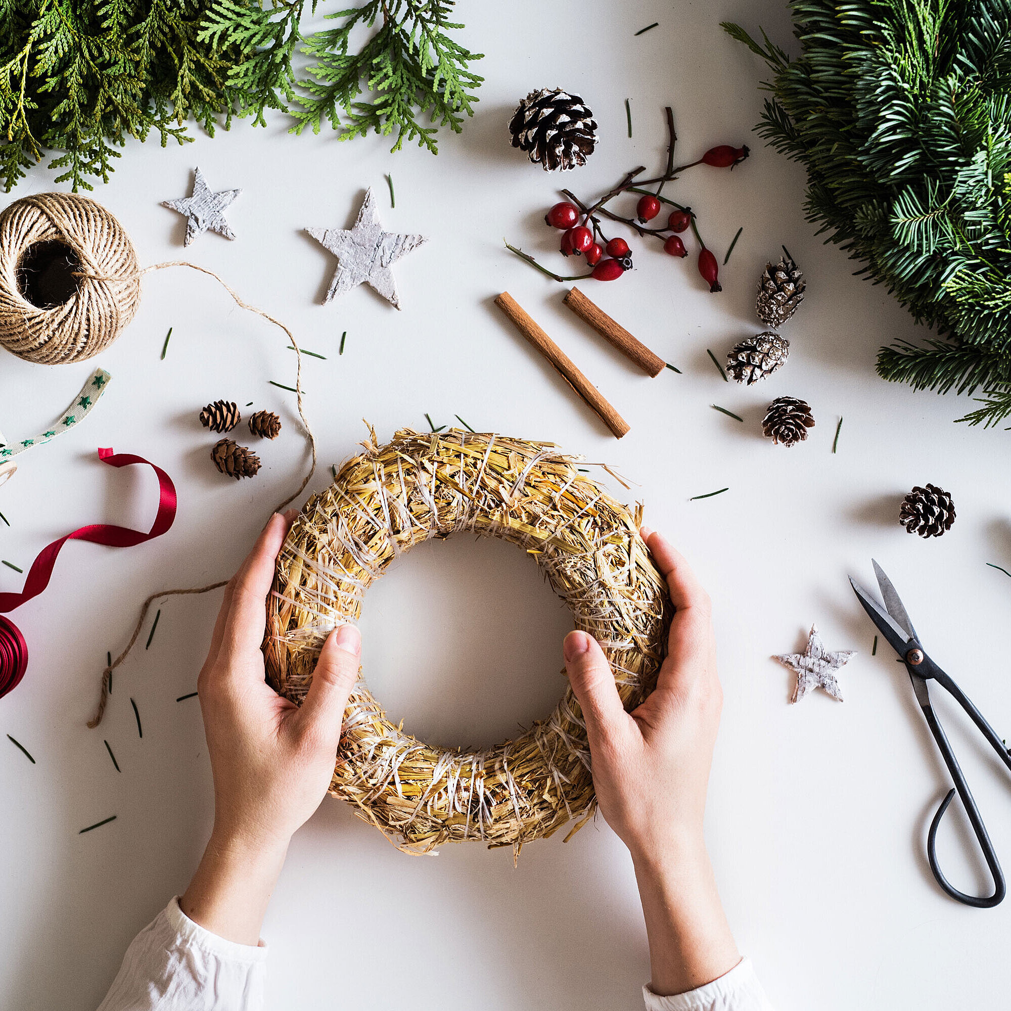 © Halfpoint - AdobeStock.com Hands arranging an Advent wreath on a table with fir branches, ribbons and craft materials.