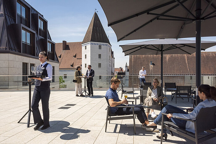 Des clients dégustent des boissons sur la terrasse sur le toit de l'hôtel Maritim Ingolstadt avec vue sur la vieille ville.