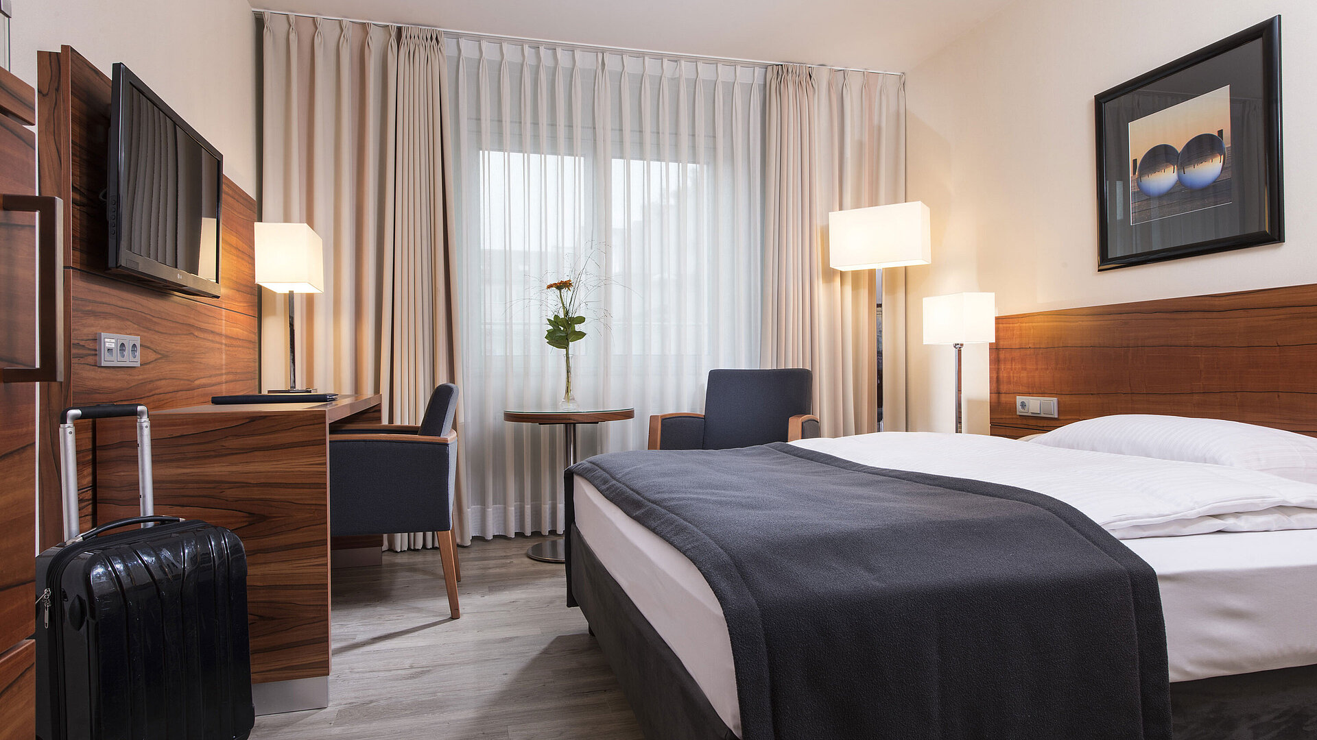 Cosy room with double bed, desk and suitcase at the Maritim Hotel Munich