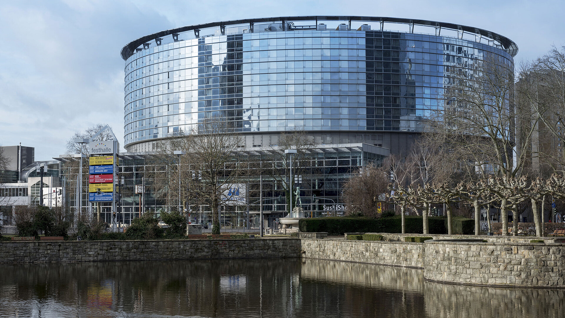 Exterior view of Maritim Hotel Frankfurt with modern glass facade and adjacent pond in daylight.
