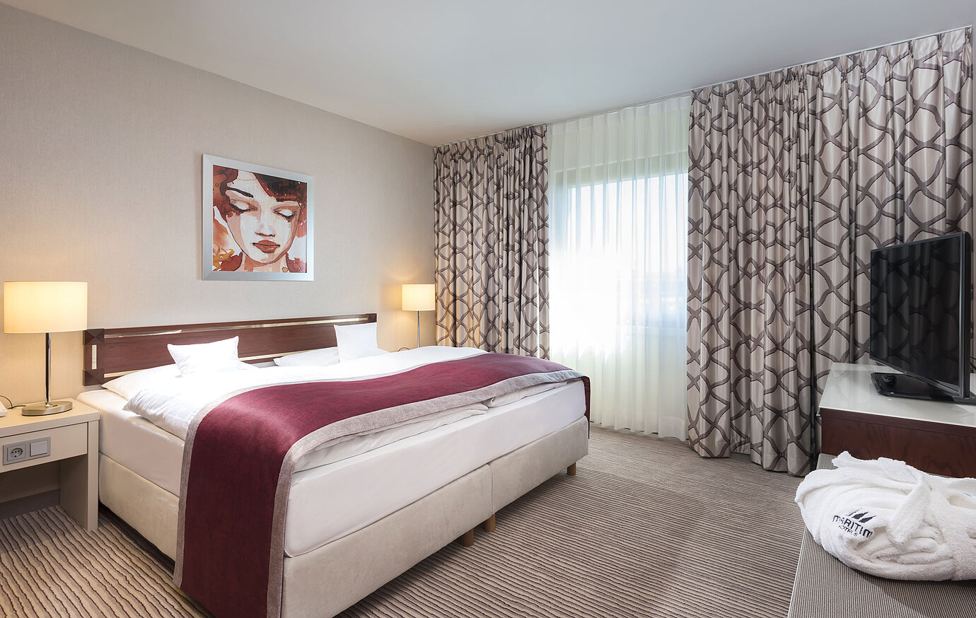 Amplia suite en el Hotel Maritim Bonn con cama doble acogedora, decoración moderna y cubrecama rojo vino.