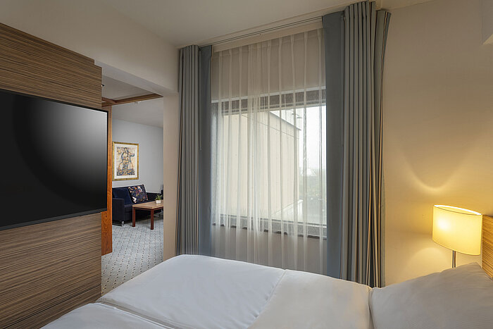 Suite junior en el hotel Maritim Darmstadt con cama cómoda, sala de estar separada y ventana de piso a techo para luz natural