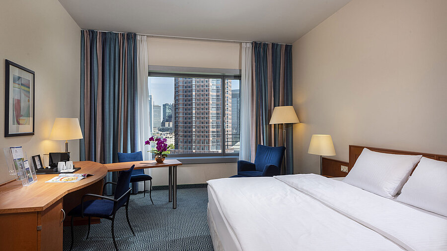 Camera Superior del Maritim Hotel Frankfurt con letto matrimoniale, scrivania e vista sullo skyline di Francoforte.