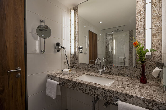 Baño moderno en el Maritim Hotel Bad Homburg con lavabo de granito, espejo e iluminación elegante.