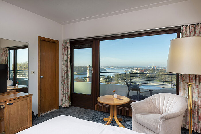 Bright hotel room with balcony, desk and view of the Trave River and Lübeck Bay