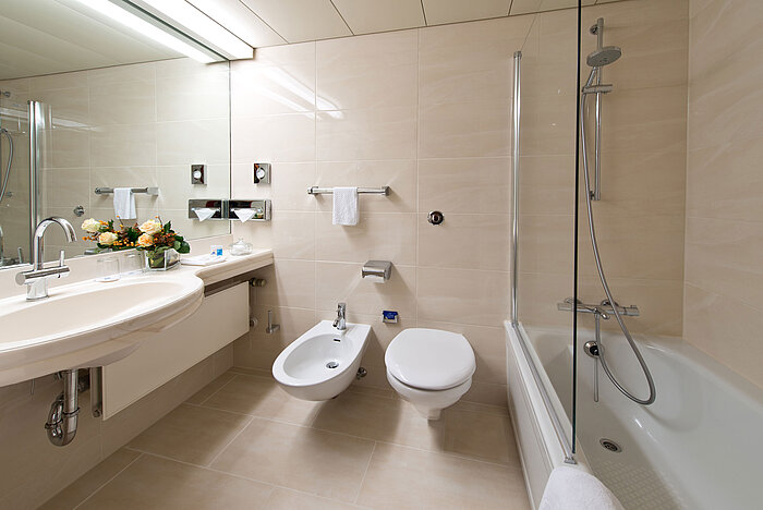 Baño elegante y luminoso con bañera, ducha, lavabo y espejo en el Maritim Hotel Hannover.