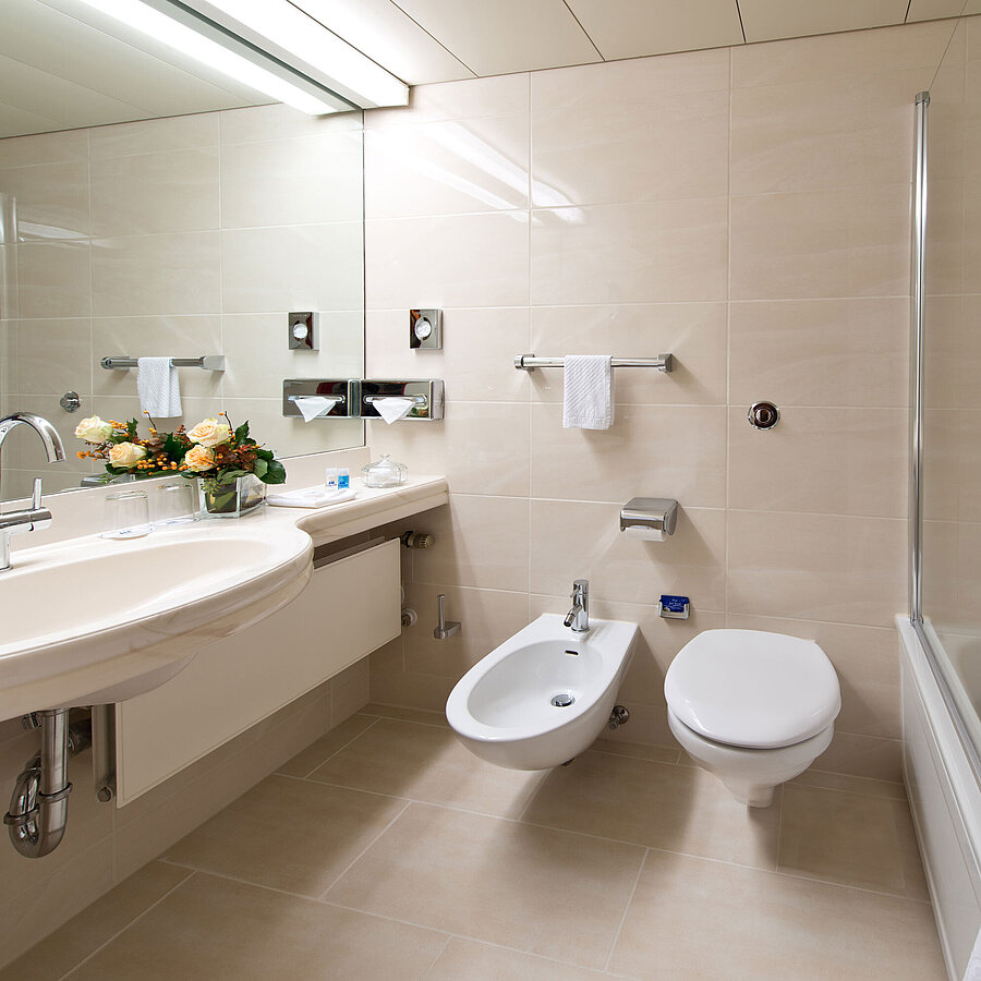 Bright, elegant bathroom with bathtub, shower, sink, and mirror at Maritim Hotel Hannover.