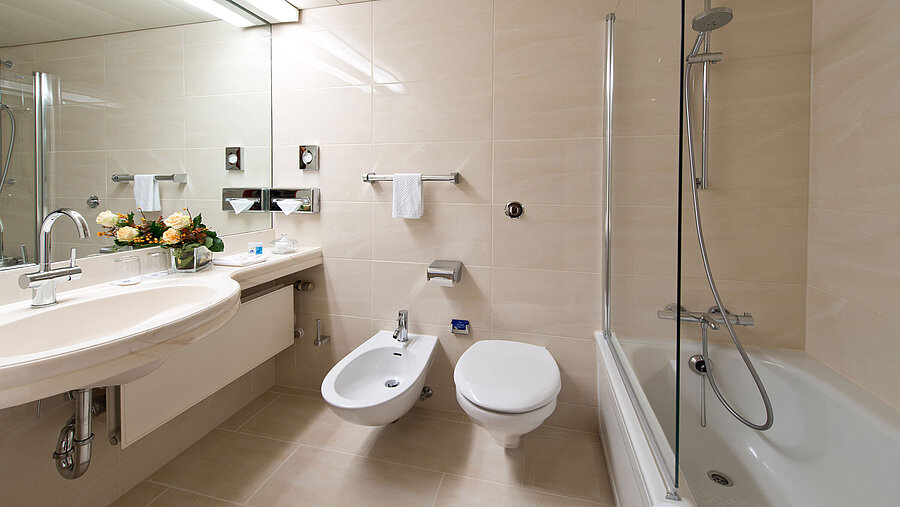 Baño elegante y luminoso con bañera, ducha, lavabo y espejo en el Maritim Hotel Hannover.