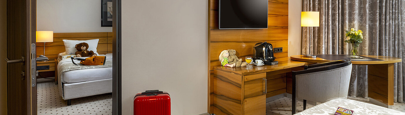 Habitación familiar Superior Habitación familiar en el Maritim Hotel Bad Homburg con cuarto separado para niños, maleta roja y oso de peluche.