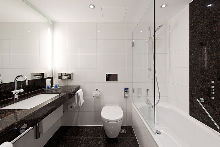 Baño moderno del Hotel Maritim Darmstadt con bañera elegante, encimera de granito oscuro y paredes claras.