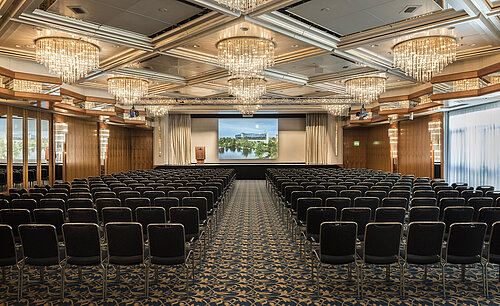 Salón de eventos elegante con lámparas de cristal, asientos en fila y un gran escenario en el Maritim Hotel Hannover.