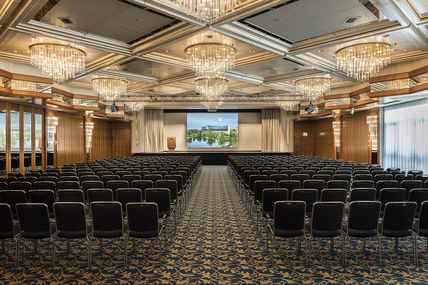 Salón de eventos elegante con lámparas de cristal, asientos en fila y un gran escenario en el Maritim Hotel Hannover.