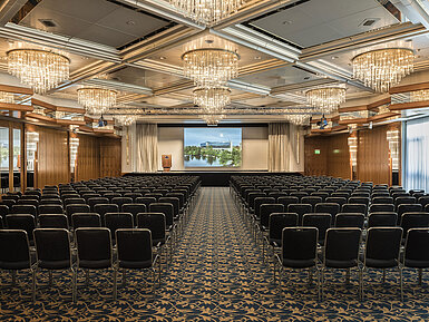 Salón de eventos elegante con lámparas de cristal, asientos en fila y un gran escenario en el Maritim Hotel Hannover.