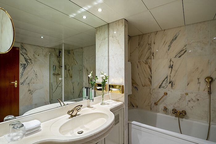 Baño moderno en Maritim Hotel Hannover con bañera, ducha de vidrio y paredes de mármol.