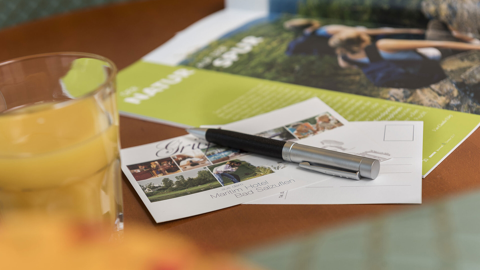 Mesa con postal del Maritim Hotel Bad Salzuflen, bolígrafo, zumo y folleto