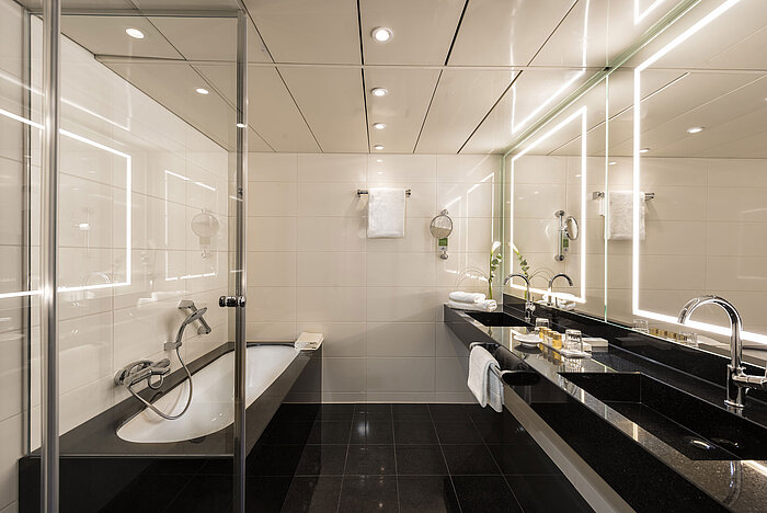 Amplio baño de suite con bañera moderna, doble lavabo e iluminación elegante en el Hotel Maritim Bonn.