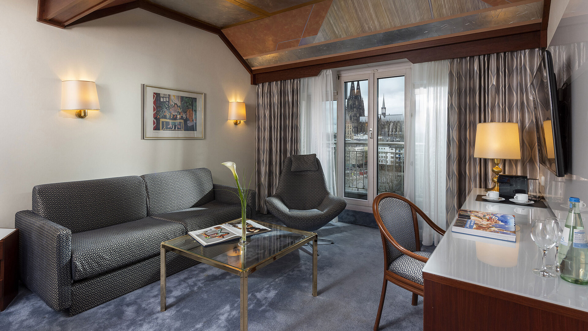 Junior Suite al Maritim Hotel Colonia con vista sulla Cattedrale di Colonia, elegante divano,poltrona e scrivania con letture