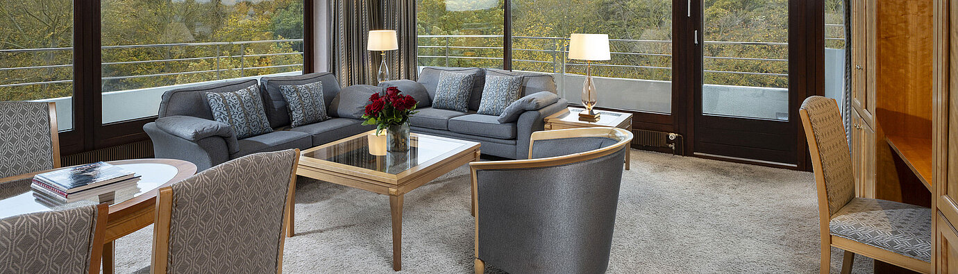 Soggiorno della Grand Suite al Maritim Hotel Kiel con ampie finestre, arredi eleganti e vista sul verde.