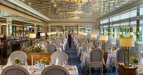 Grande ristorante elegante con lunghe tavole apparecchiate, lampadari e composizioni floreali per cene raffinate.