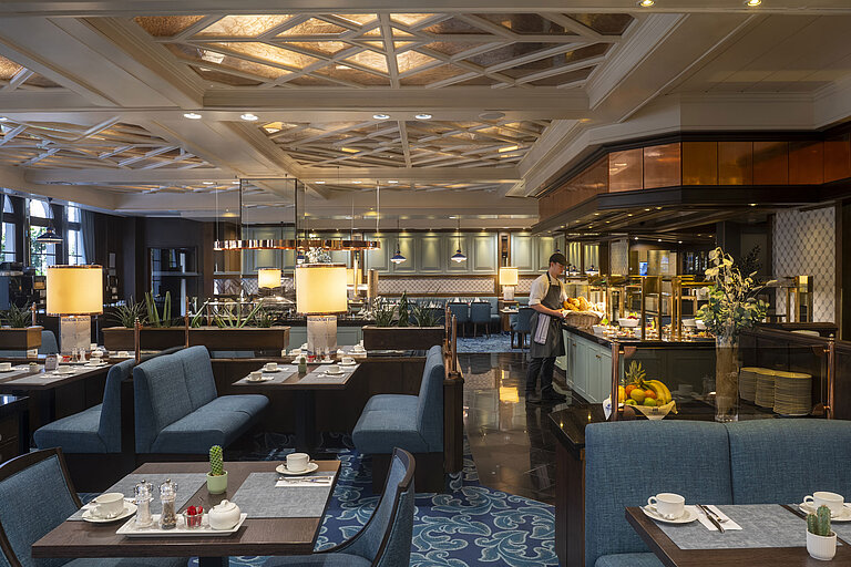 Restaurante del hotel Maritim Darmstadt con mesas preparadas, área de buffet e iluminación elegante bajo un techo artístico.