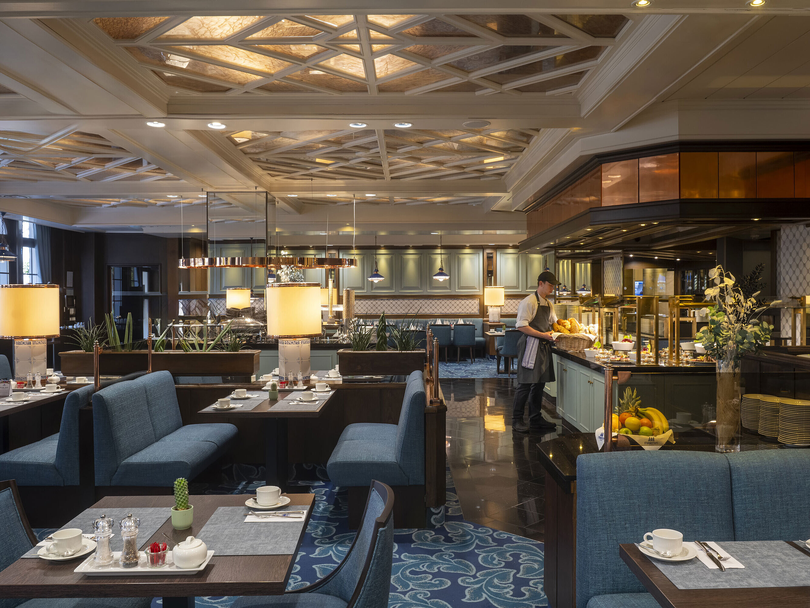 Restaurant at the Maritim Hotel Darmstadt with set tables, buffet area, and elegant lighting under an artistic ceiling.