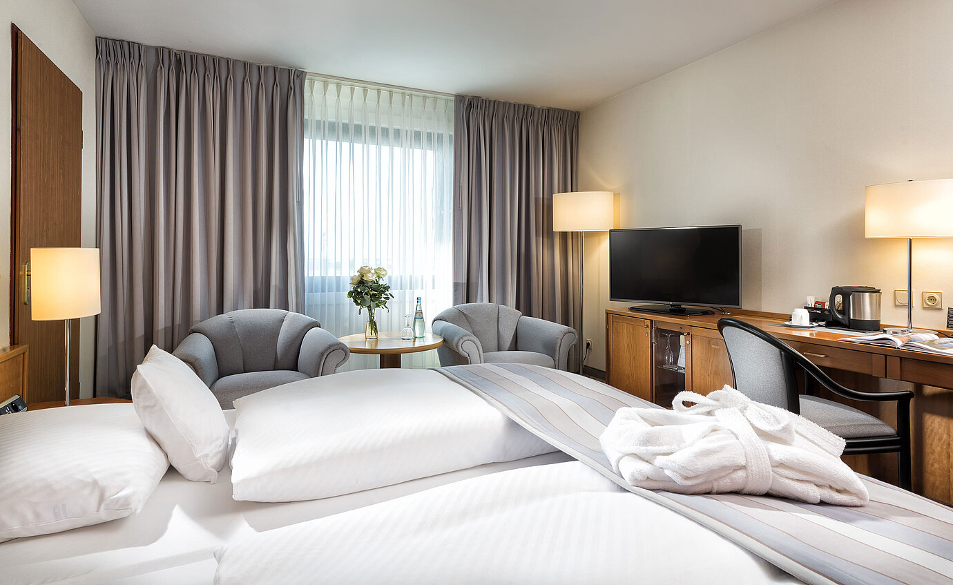 Habitación doble superior con mobiliario elegante, acogedora zona de estar, botellas de agua y albornoz sobre la cama.