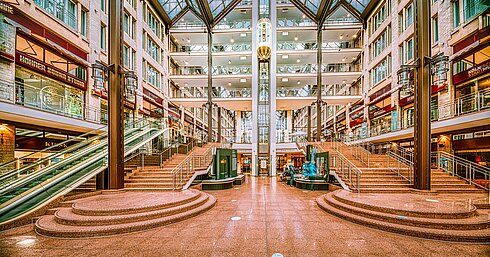 El espacioso vestíbulo del Hotel Maritim con escaleras, escaleras mecánicas, techo de cristal y tiendas en varios niveles.
