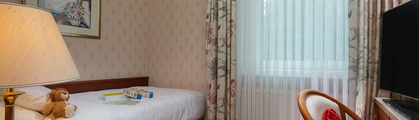 Camera familiare Comfort con letto singolo, giocattoli, area salotto e ampia finestra per un soggiorno accogliente.