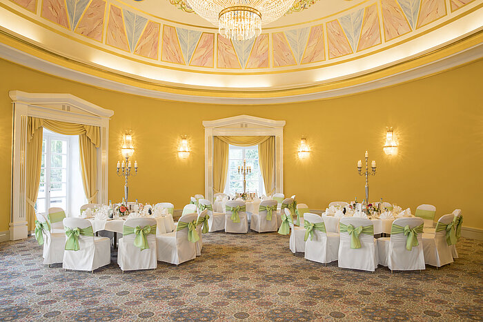 Salle de réception élégante avec murs jaunes, tables rondes et chandeliers au Maritim Hotel Bad Wildungen