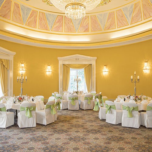 Salón elegante con paredes amarillas, mesas redondas y candelabros en el Maritim Hotel Bad Wildungen