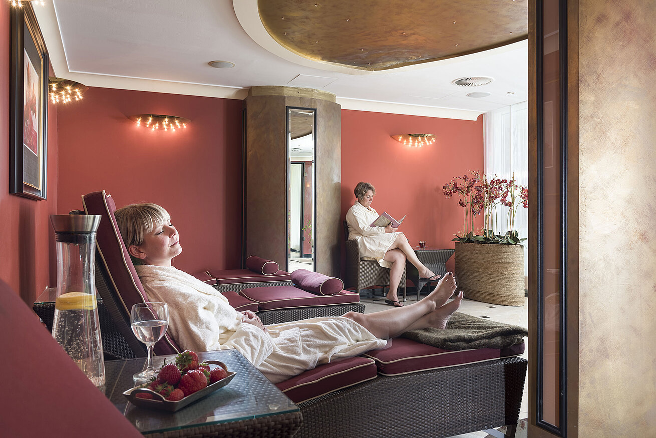 Sala relax con pareti rosse al Maritim Seehotel Timmendorfer Strand, ospiti rilassati sui lettini.