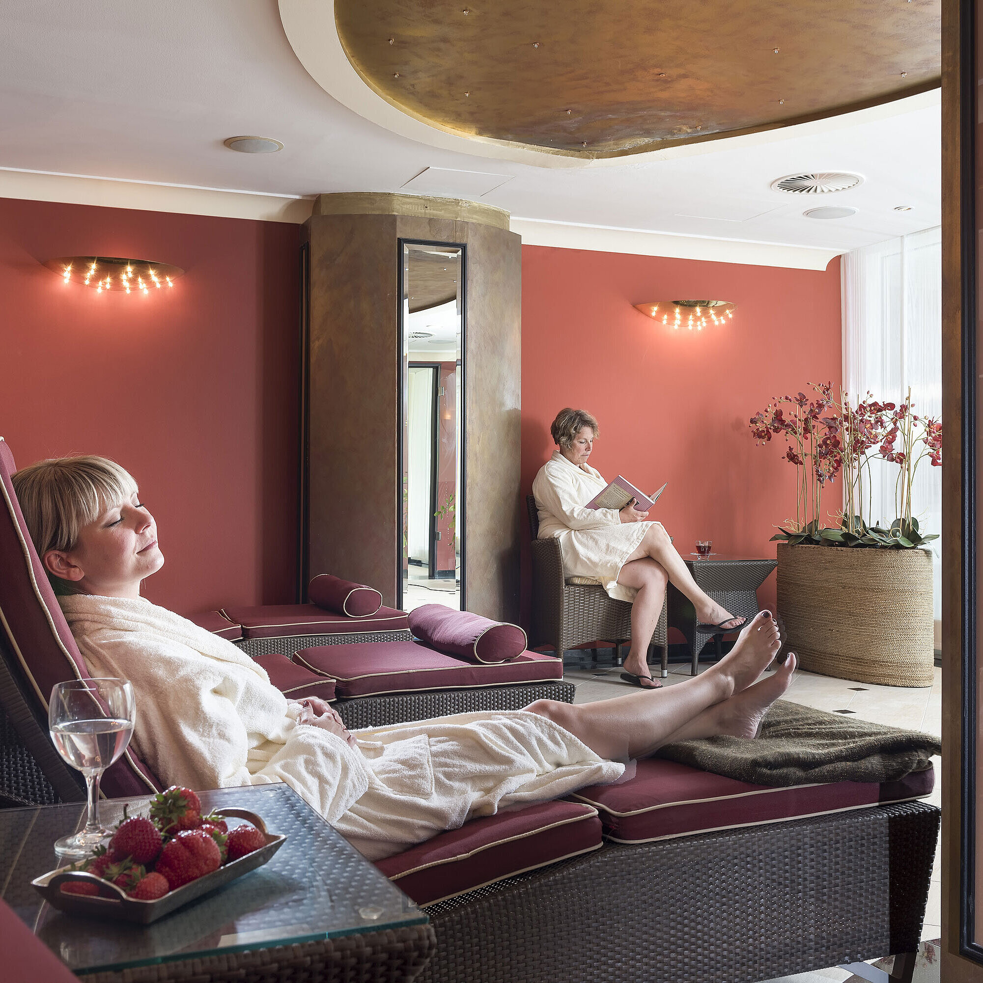 Sala de descanso con paredes rojas en Maritim Seehotel Timmendorfer Strand, huéspedes relajándose en tumbonas.