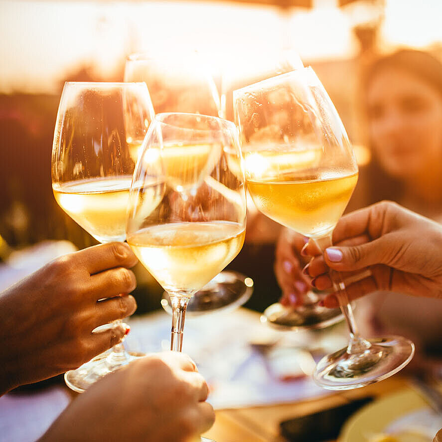 Friends clinking wine glasses while enjoying an evening together at sunset