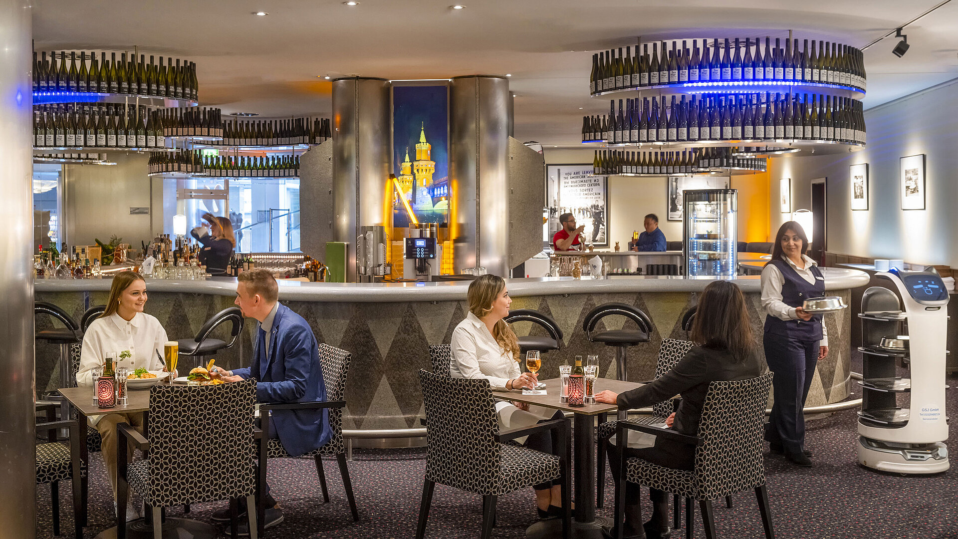 Guests dining at the bar of the Maritim proArte Hotel Berlin, surrounded by modern facilities and a service robot.