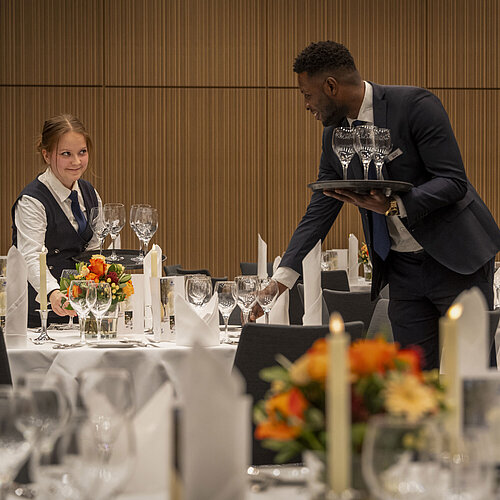 El personal de servicio prepara las mesas en el Salón Barbarossa del Maritim Hotel Würzburg con decoración floral y copas.
