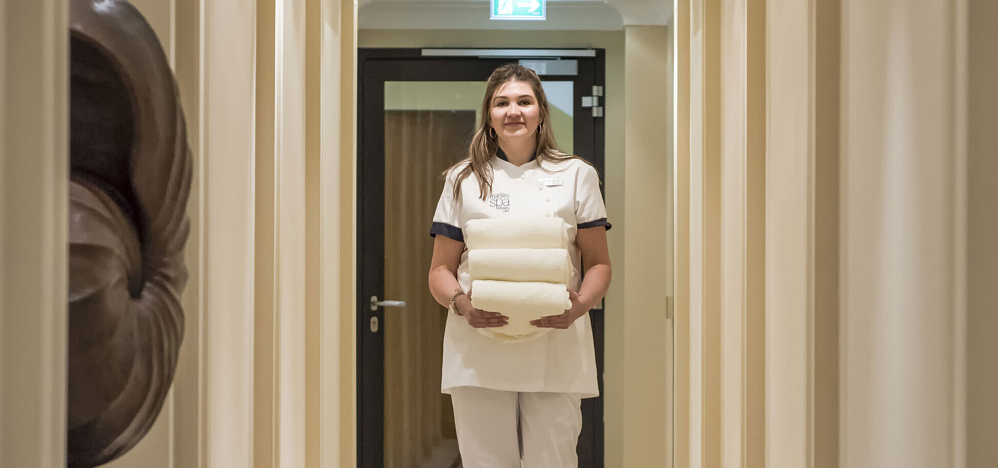 Miembro del personal de bienestar en el área de spa del Hotel Maritim, llevando toallas en un elegante pasillo.