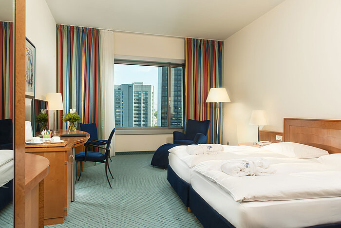 Chambre supérieure à l'hôtel Maritim Frankfurt avec lit double, bureau, coin salon et vue sur la skyline.