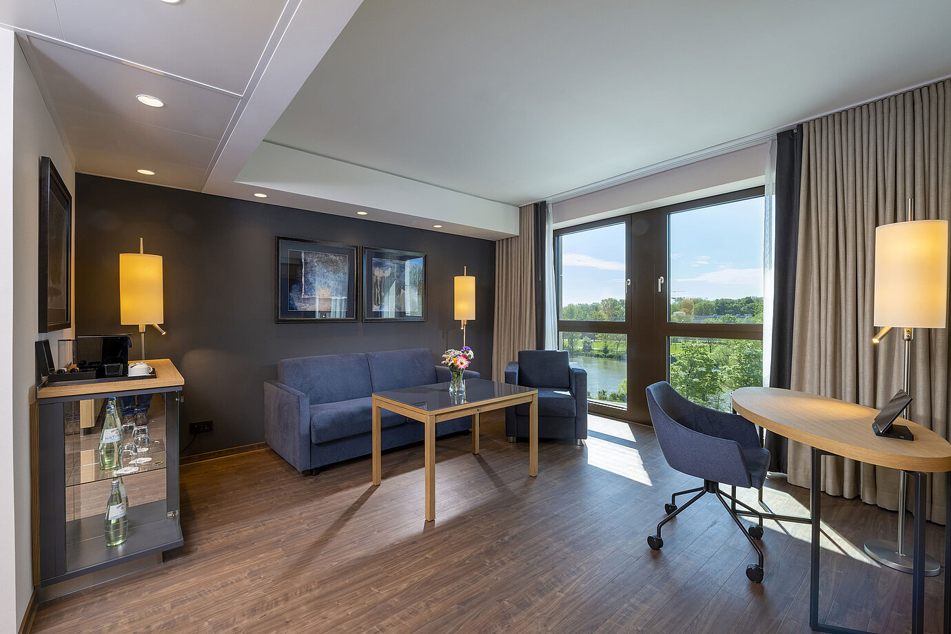 Bright suite with seating area, large window, and nature view at Maritim Hotel Ingolstadt.