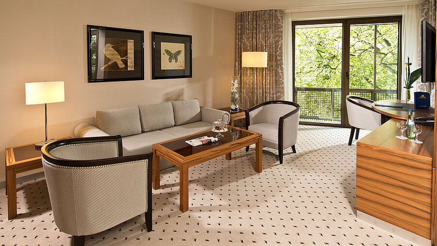 Zona giorno accogliente della suite all'hotel Maritim Bad Homburg con salotto elegante e balcone.
