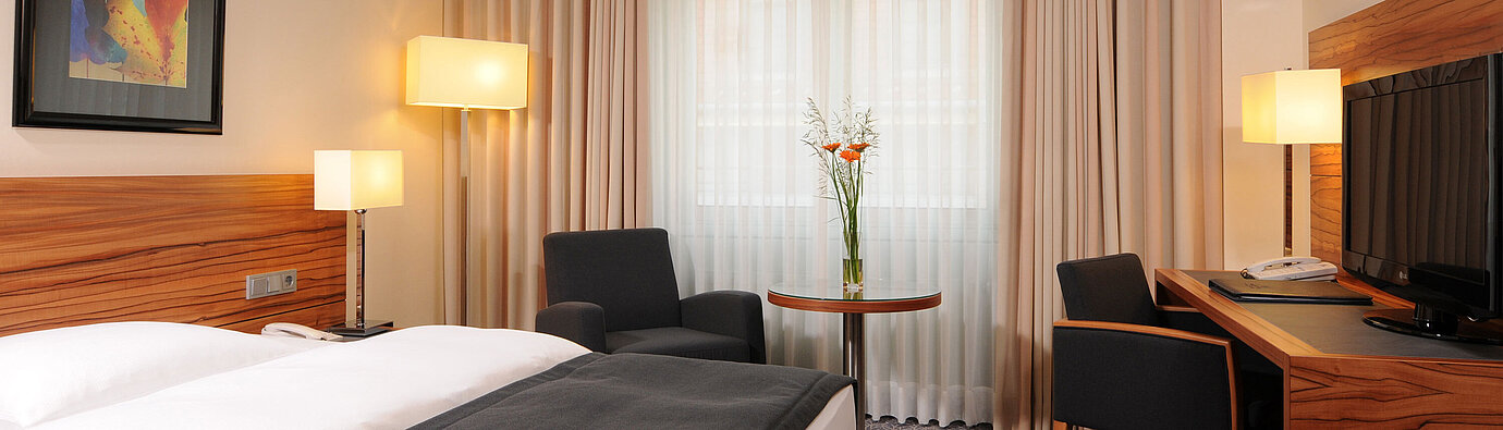Habitación individual moderna con cama, sillones y gran ventana en Maritim Hotel Múnich