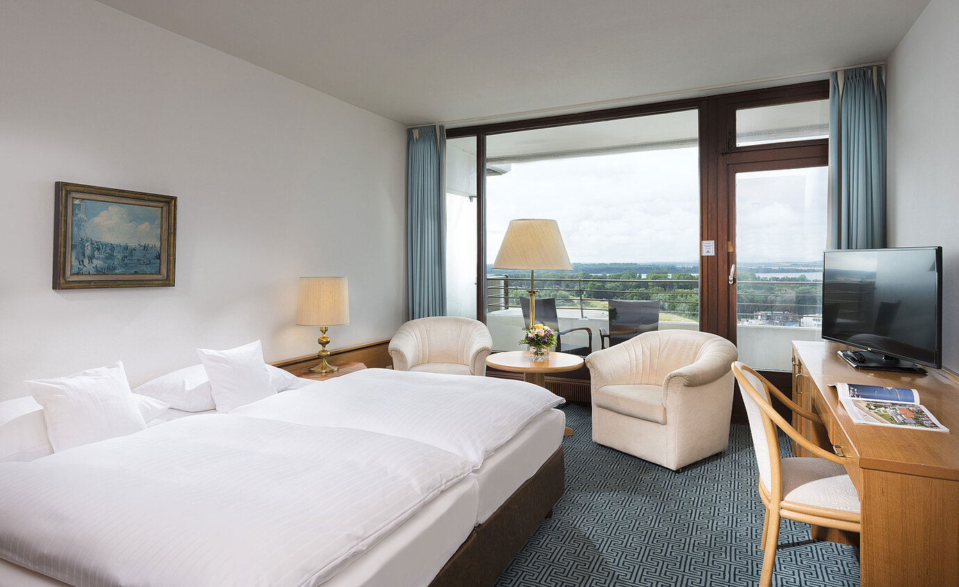 Double room with seating area, desk and balcony overlooking green landscape in Travemünde