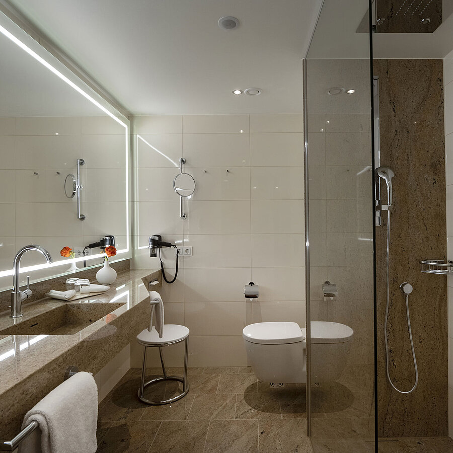 Bathroom at Maritim Hotel Ingolstadt with glass shower, large mirror, and stylish design.