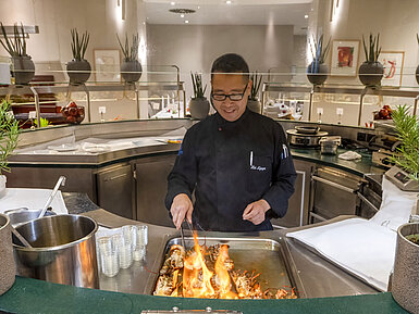 Chef at Maritim proArte Hotel Berlin flambéing dishes at the live cooking station in front of guests.