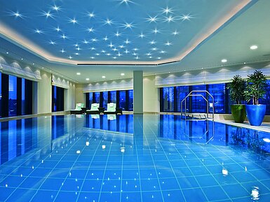 Illuminated indoor pool at Maritim Hotel Düsseldorf with modern loungers and panoramic windows, perfect for relaxation.