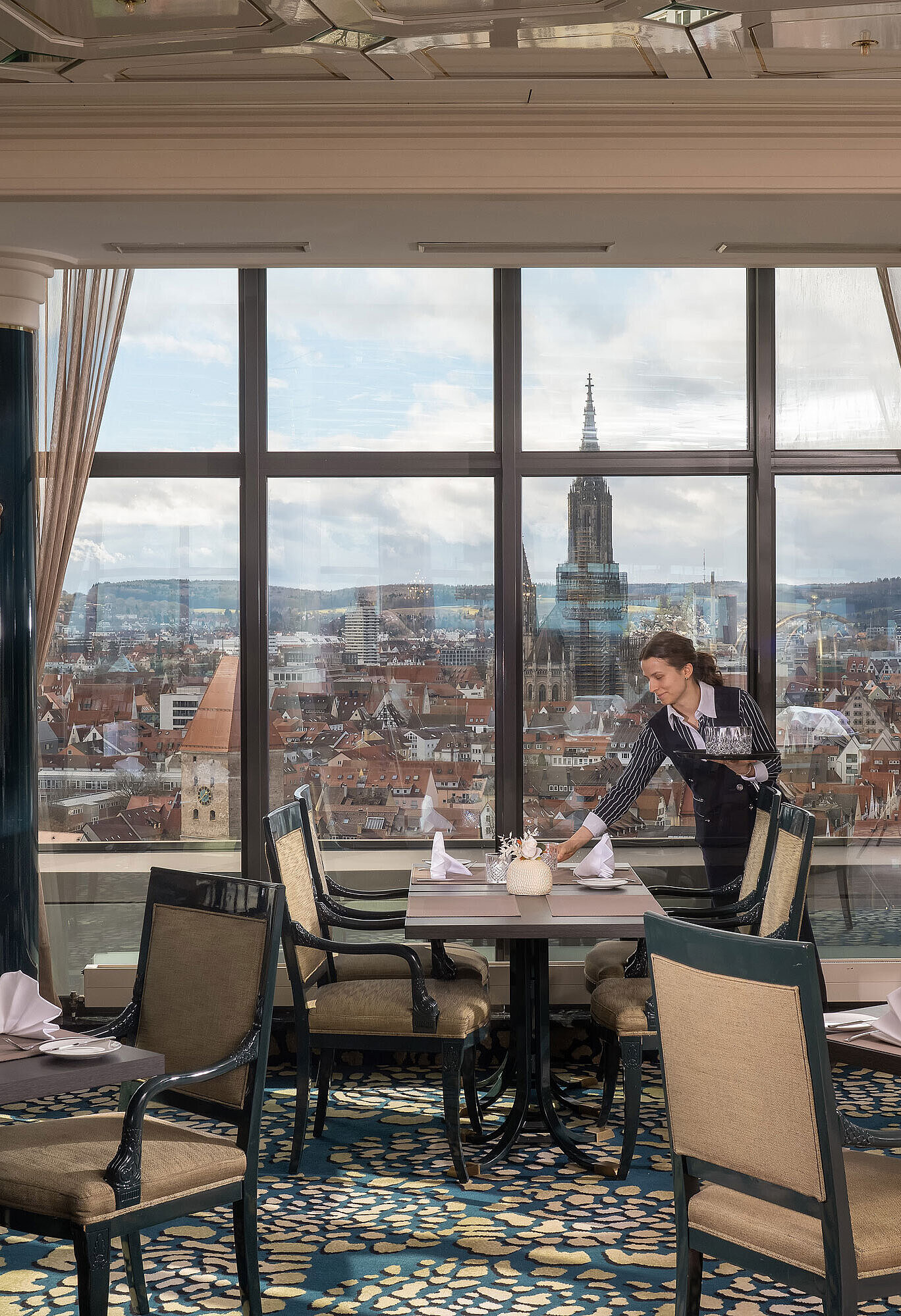 Restaurante en Maritim Hotel Ulm con mesas preparadas, grandes ventanales y vistas a Ulm y la catedral de Ulm