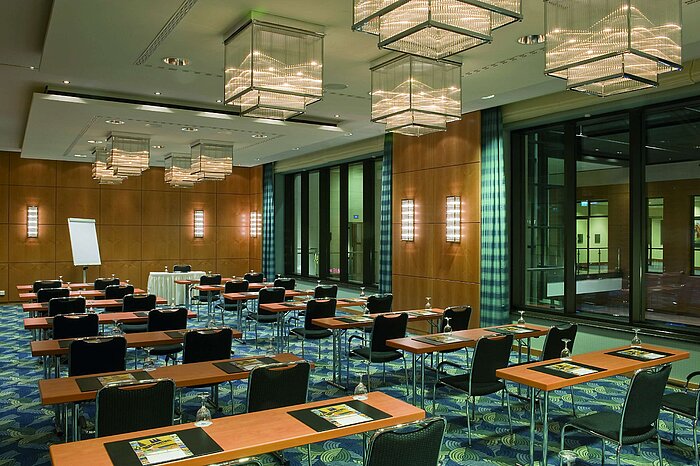 Sala de conferencias moderna con elegantes candelabros, paredes de madera y grandes ventanales en el Maritim Hotel.