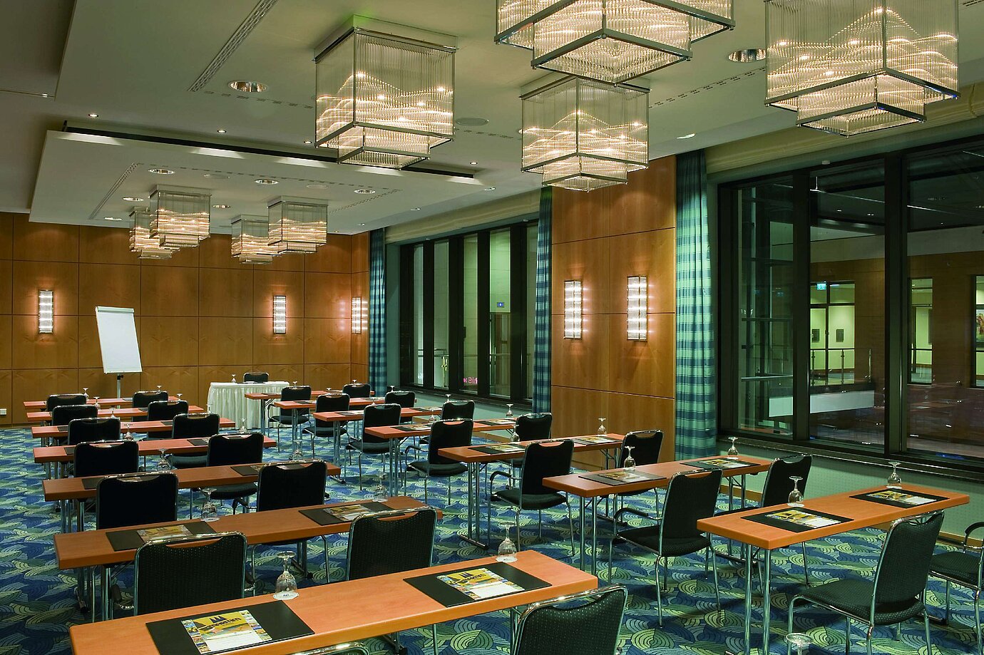 Sala de conferencias moderna con elegantes candelabros, paredes de madera y grandes ventanales en el Maritim Hotel.