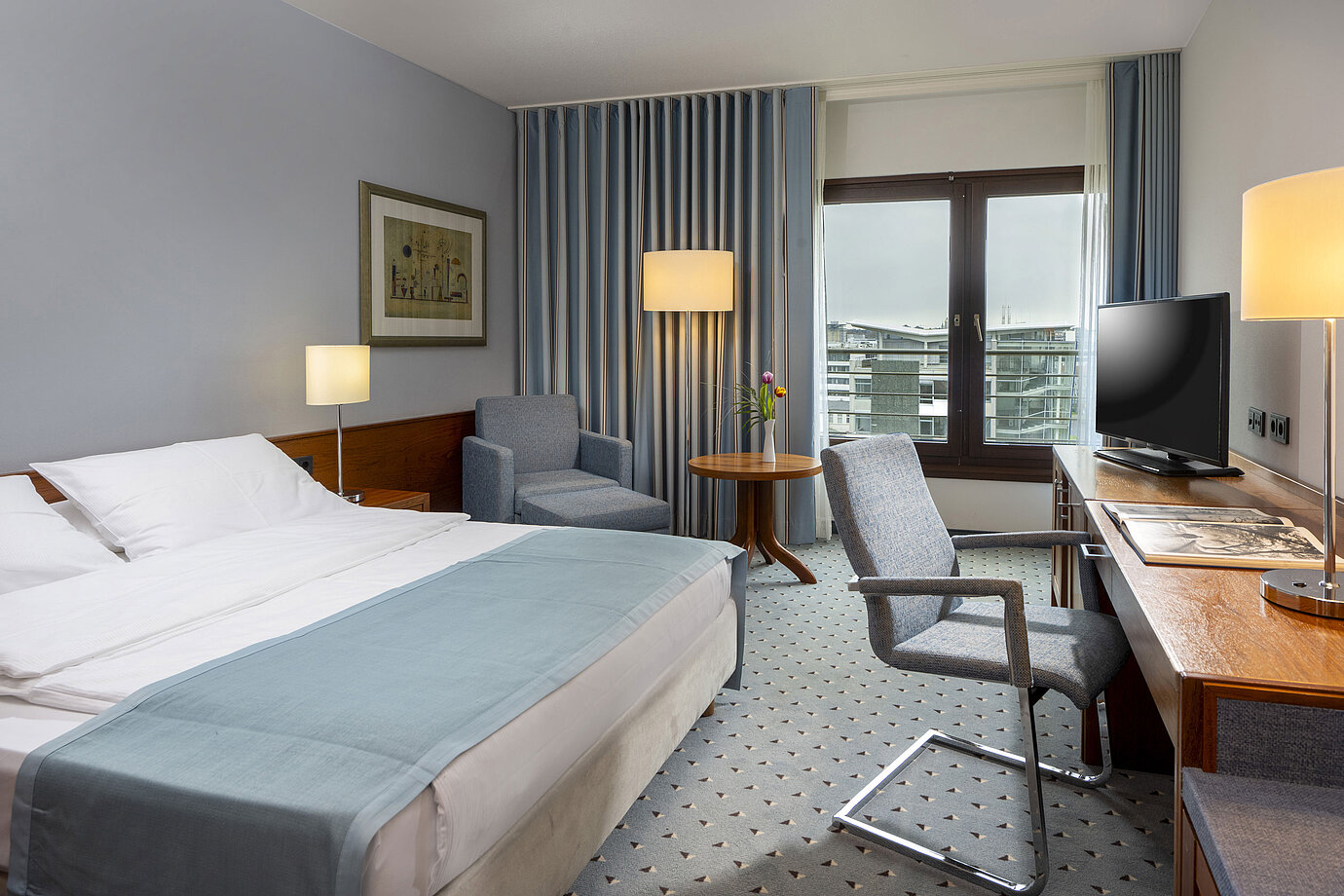 Habitación doble confort en el Hotel Maritim Darmstadt con área de estar acogedora, escritorio moderno y vista a la ciudad.