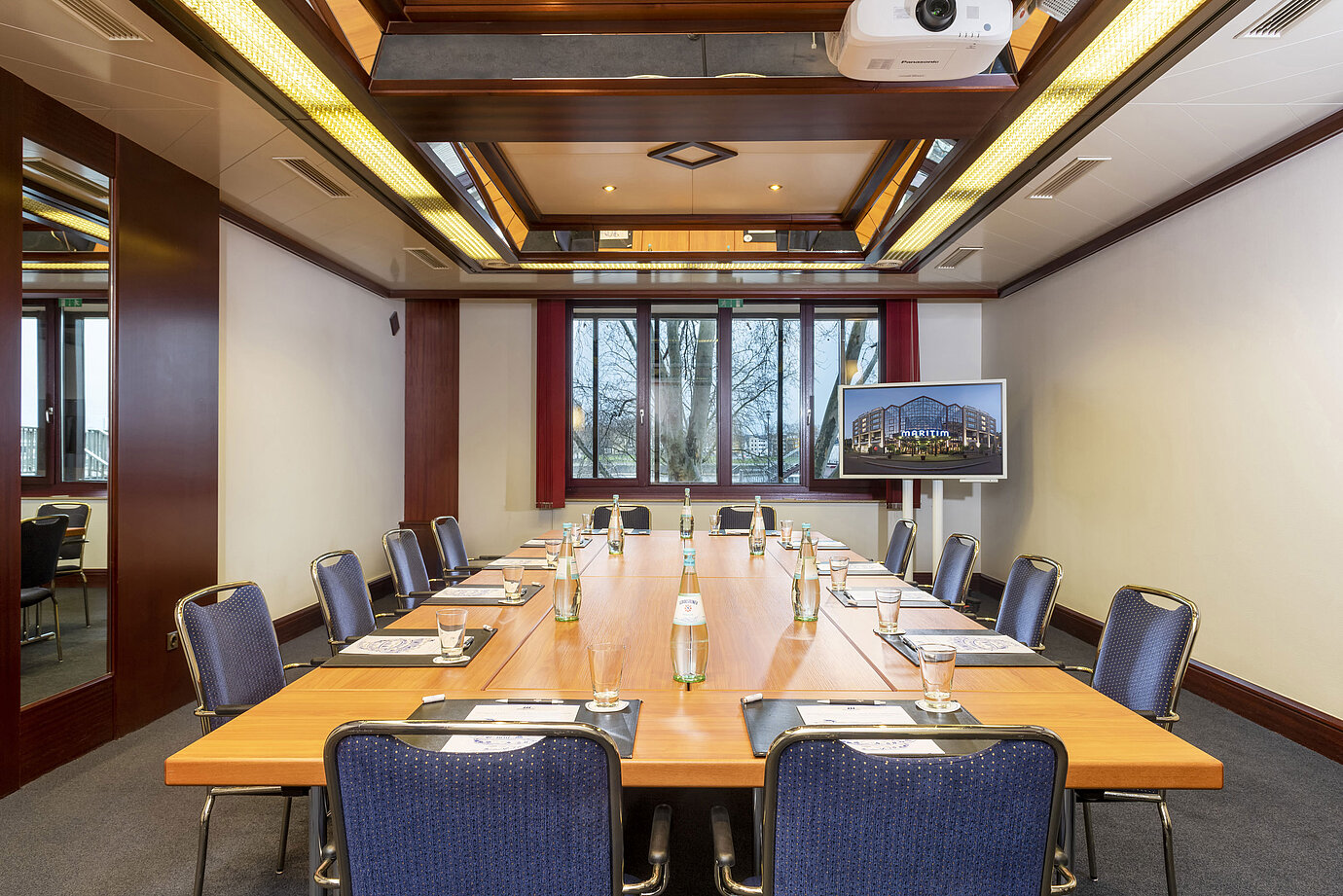 Salón Loreley, una moderna sala de conferencias con disposición cuadrada, proyector y pantalla para presentaciones.